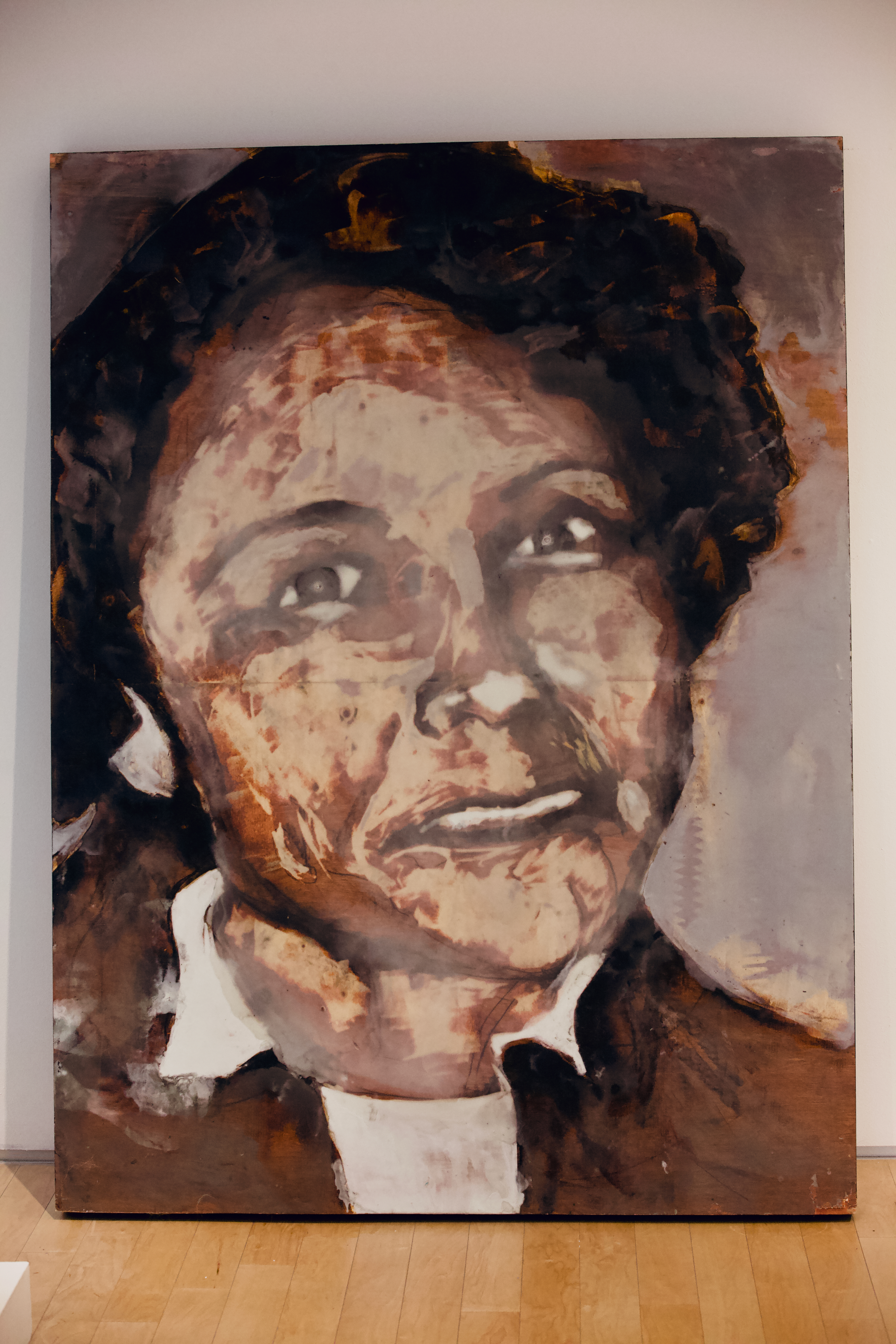 A large rust-toned portrait leaning against a gallery wall