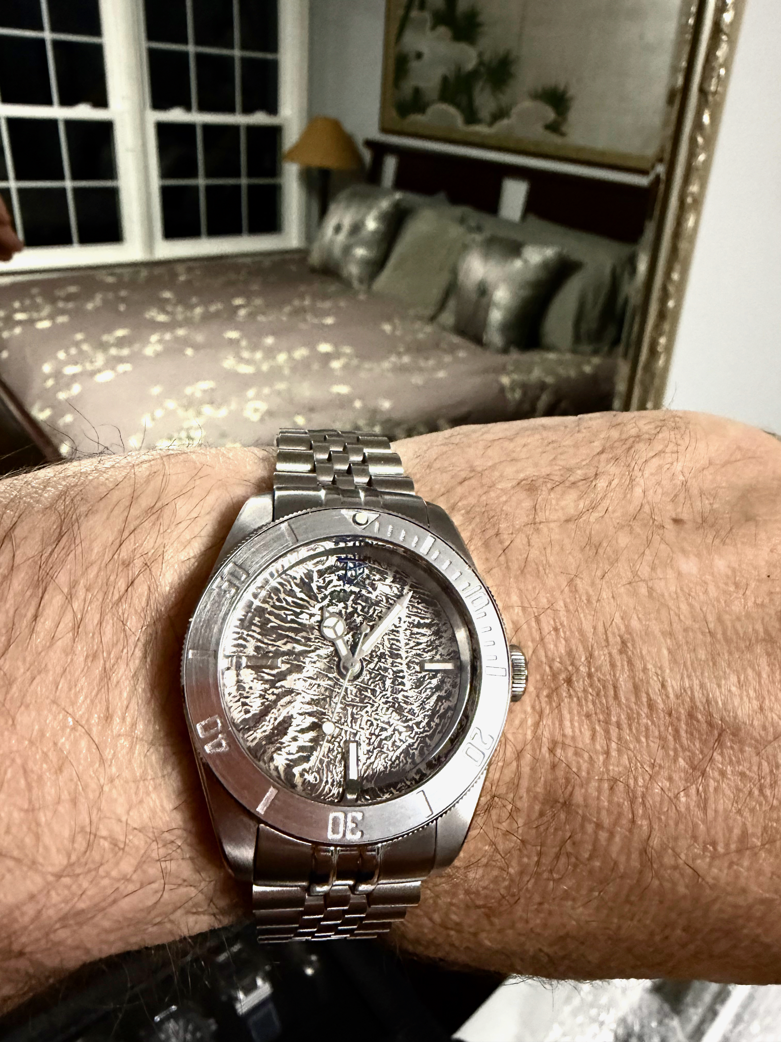 A bare reticulated silver dial in a dive case on a jubilee bracelet