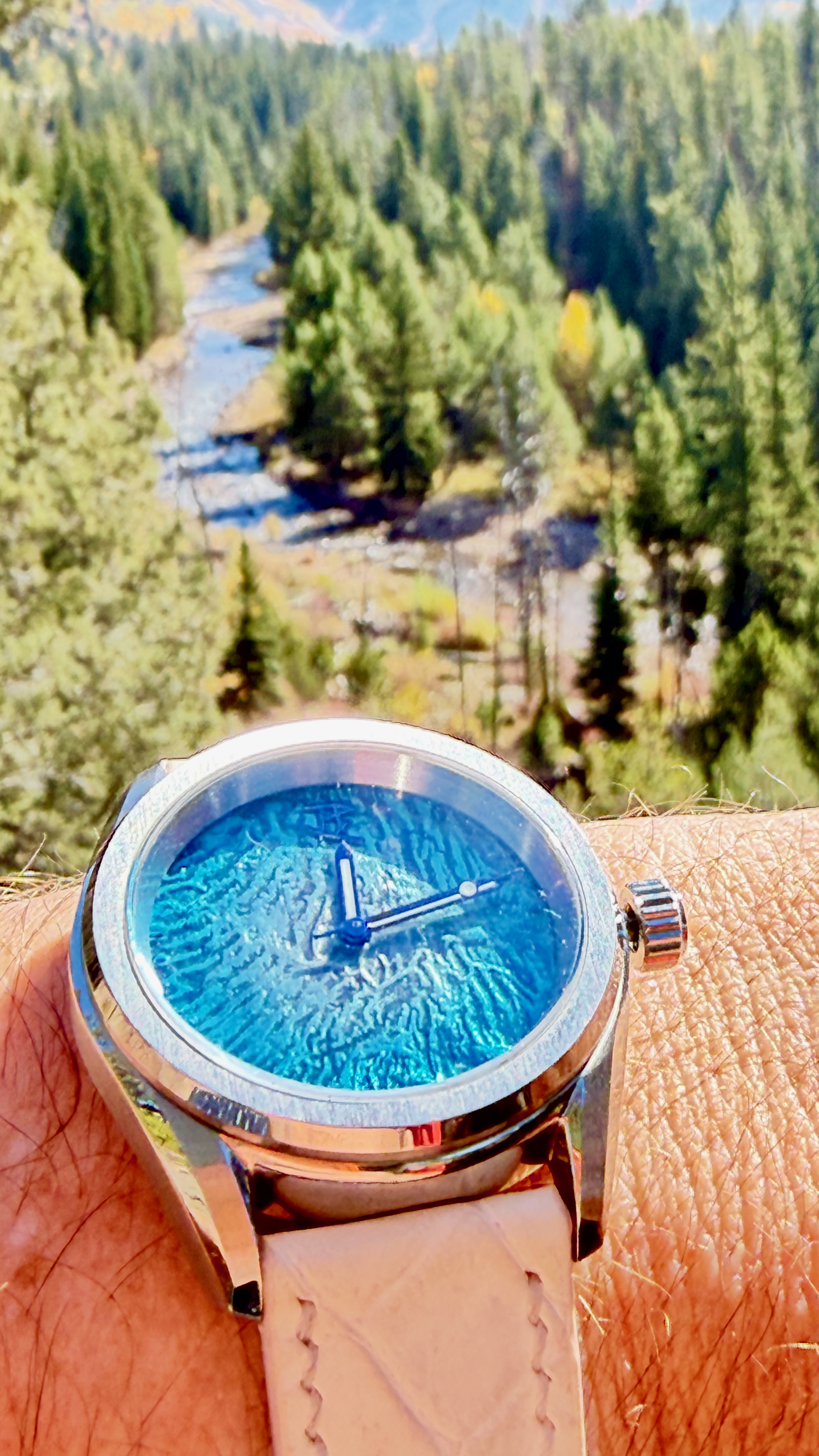 The turquoise enamel dial on a blush leather strap, a river valley below
